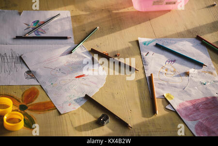 Various kid's drawings on paper and accessories on table. Stock Photo