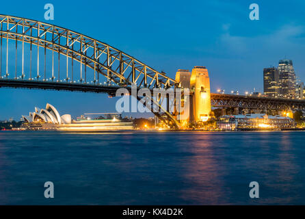 Night panorama of Sydney Harbour, Australia. Cityscape at night, Sydney Harbour Bridge, ferry passes in front of Opera House. Stock Photo