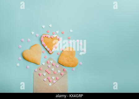 Open craft paper envelope with fly out sugar candies and heart shaped homemade cookies on light blue background. Valentine day. love concept. Gift, me Stock Photo