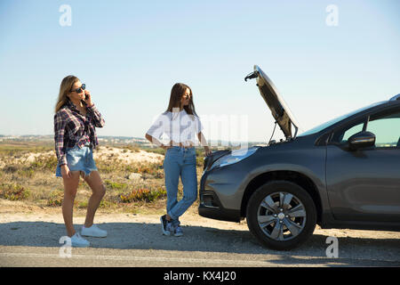 Female friends examining broken down car on country road Stock Photo