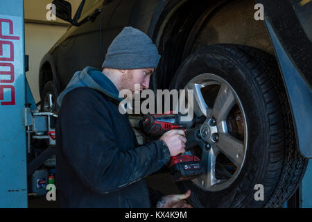 Young Apprentice mechanic removing a car wheel with a cordless impact wrench Stock Photo