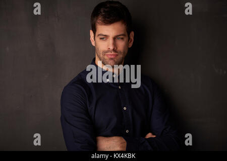 Thinking young man standing with arms crossed at dark background. Stock Photo