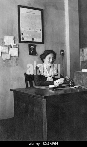 Historical photo of a woman seated at a small wooden office desk, circa 1910. Stock Photo