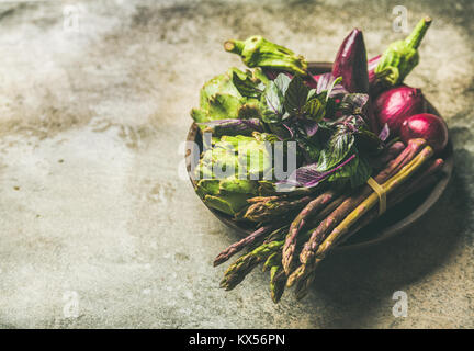 Flat-lay of green and purple vegetables on plate, concrete background Stock Photo