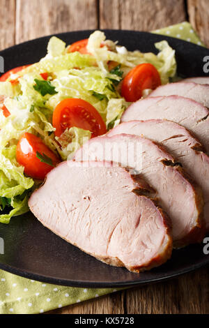 Sliced roast pork tenderloin with vegetable salad close-up on a plate on a table. vertical Stock Photo
