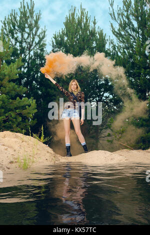 Lost hiker wagging smoke flare to signal for help on outer wood standing by the lake Stock Photo