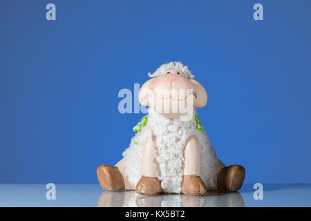 Figurine of a small funny sitting sheep blue background Stock Photo