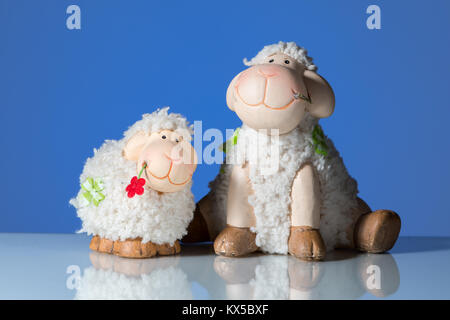 Figurines of two funny sheep in front of a blue background, reflective surface Stock Photo