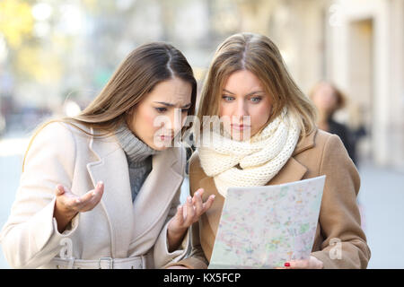 Front view portrait of two lost tourists women searching location in a guide on the street in winter holidays Stock Photo