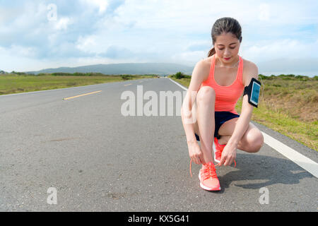 smiling attractive runner tying shoelace on road. Stock Photo