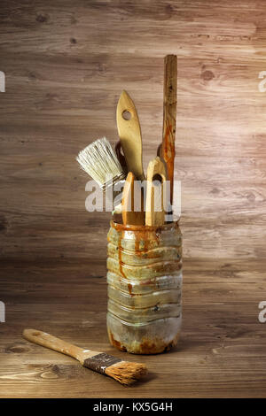 used paintbrushes in a plastic jar on a rustic wooden background Stock Photo