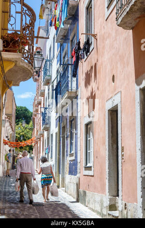 Lisbon Portugal,Alfama,historic neighborhood,narrow street,cobblestone,alley,man men male,woman female women,walking,carrying bags,Hispanic,immigrant Stock Photo