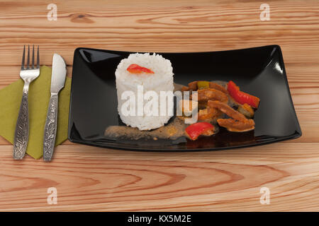 Soy noodles and rice with tomatoe sauce, paprika, cucumber and milk cream, on black plate on wooden table. Stock Photo