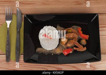 Soy noodles and rice with tomatoe sauce, paprika, cucumber and milk cream, on black plate on wooden table. Stock Photo