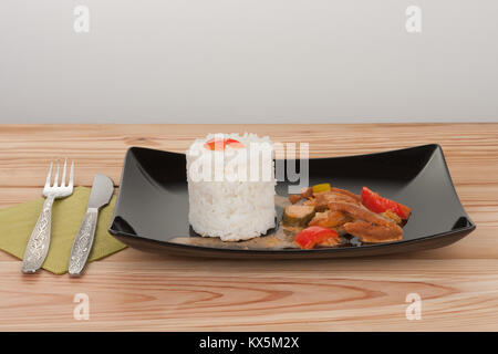 Soy noodles and rice with tomatoe sauce, paprika, cucumber and milk cream, on black plate on wooden table. Stock Photo