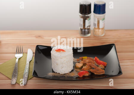 Soy noodles and rice with tomatoe sauce, paprika, cucumber and milk cream, on black plate on wooden table. Stock Photo