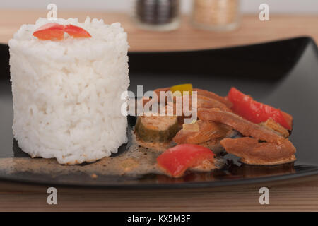 Soy noodles and rice with tomatoe sauce, paprika, cucumber and milk cream, on black plate on wooden table, close up view. Stock Photo