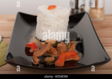 Soy noodles and rice with tomatoe sauce, paprika, cucumber and milk cream, on black plate on wooden table. Stock Photo