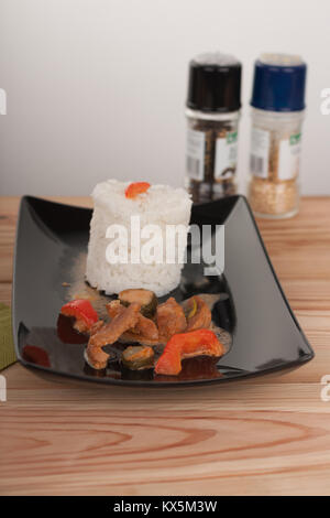 Soy noodles and rice with tomatoe sauce, paprika, cucumber and milk cream, on black plate on wooden table. Stock Photo