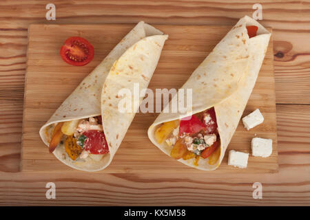 Tortilla wraps with chicken meat, tomato, french fries and feta cheese, traditional greek fast food called souvlaki or gyros in pita. Stock Photo