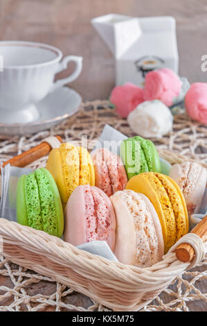 Freshly baked macarons in a wicker basket with marshmallows and a Cup of tea. Stock Photo