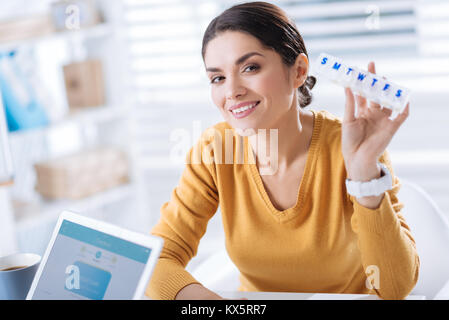 Smiling woman holding a useful pillbox and feeling glad to recover Stock Photo