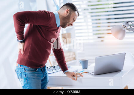 Exhausted man leaning to the table while suffering from backache Stock Photo