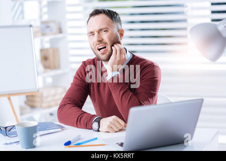 Unhappy man feeling terrible toothache while working in his office Stock Photo