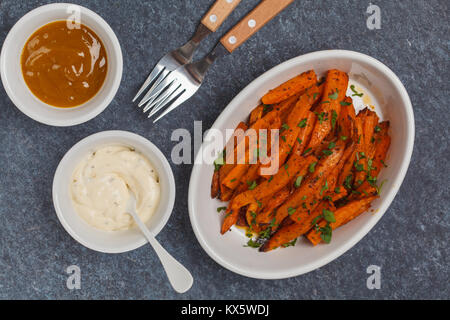 Healthy baked sweet potato fries with curry and creamy garlic sauces. White utensils, dark background, top view. Stock Photo