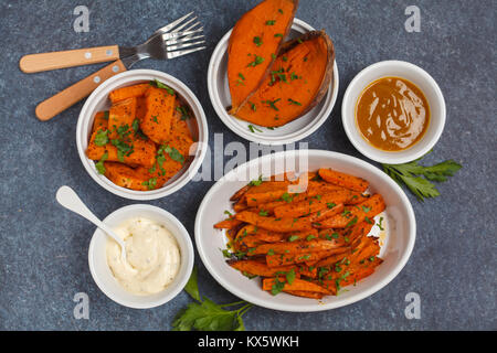 Different types of baked sweet potato with curry and a creamy garlic sauce. Healthy vegan food concept. Stock Photo