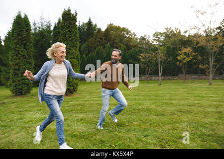 Cheerful mature couple holding hands while running together outdoors Stock Photo