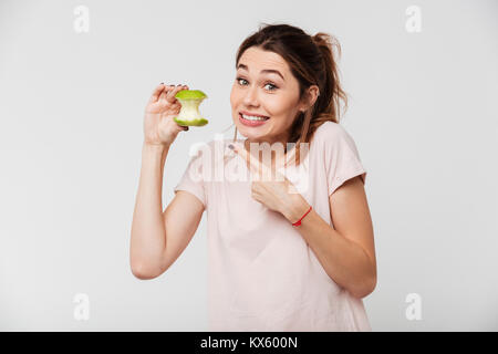 Portrait of a smiling silly girl pointing finger at a half eaten apple isolated over white background Stock Photo