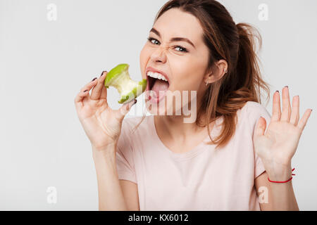 Close up portrait of a hungry pretty girl biting an apple isolated over white background Stock Photo