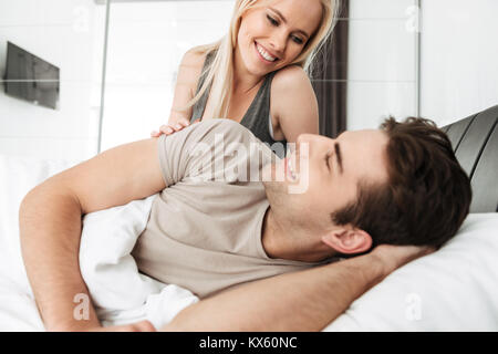 Young smiling blonde lady looking at her cheerful husband while lying in bed Stock Photo