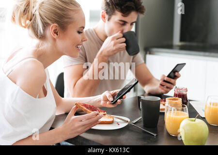 Pretty concentrated lovers using their smarrtphones while eating breakfast in kitchen Stock Photo