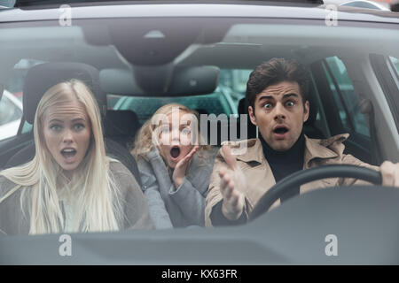 Image of shocked scared young man sitting in car with his wife and daughter. Looking camera. Stock Photo