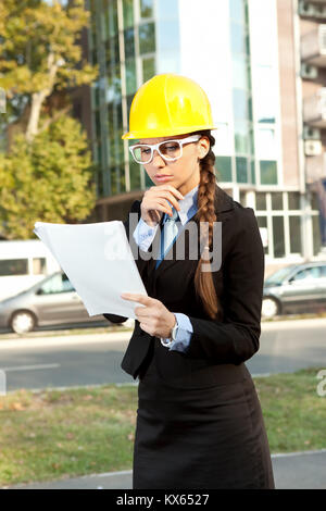 Woman in yellow hard hat,  reading notes while standing Stock Photo