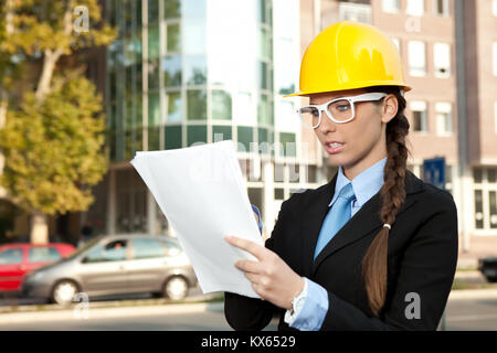 female engineer looking at blueprints in construction site Stock Photo