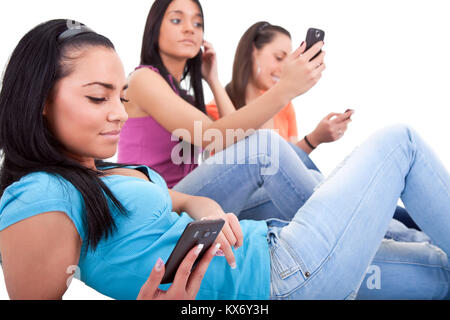 three young girls texting on their cell phones, isolated white background Stock Photo