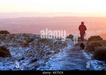 Flintshire, Wales, UK. 8th Jan, 2018. UK Weather: Another clear night for many and once again widespread freezing temperatures. A lone walker with two dogs walkign along a footpath the contours the Iron Age Hillfort of Moel-y-Gaer on Halkyn Mountain in Flintshire as the sun breaks the horizon and floods the beautiful landscape with colour Credit: DGDImages/Alamy Live News Stock Photo
