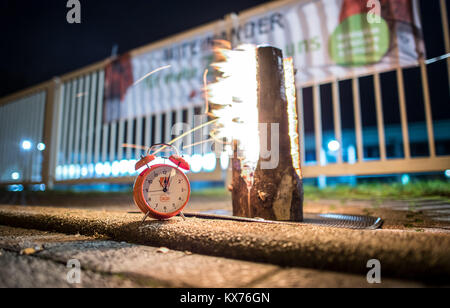 Iserlohn, Germany. 08th Jan, 2018. An alarm clock of the IG Metall stands next to a burning log at a kick-off warning strike assembly in front of the factory gates of Kirchhoff Automotive (Kirchhoff Witte) in Iserlohn, Germany, 08 January 2018. The IG Metall (Industrial Union of Metalworkers) wants to exert pressure on the employers prior to the third round of negotiation on 18 January. Therefore, they called thousands of metalworkers from more than 500 companies to strike Credit: Guido Kirchner/dpa/17�Թ����� Live News Stock Photo