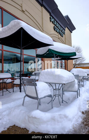 Empty Starbucks Coffee sidewalk patio tables, chairs, and umbrellas covered by fresh snow, winter scene, London, Ontario, Canada Stock Photo