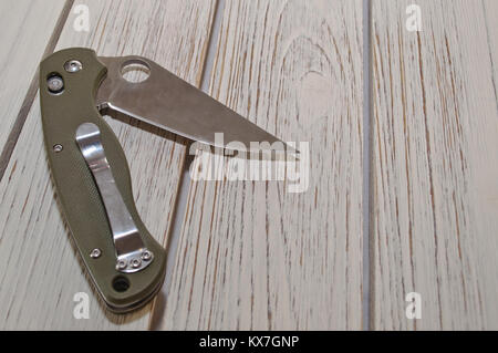 An opened folding pocket knife with a green handle laying on a white wooden table Stock Photo