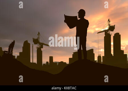 Silhouette of working man standing with his planning paper and crane in construction site at sunset Stock Photo