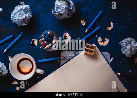 Open notepad with blank pages, crumpled paper balls, pencils, notepads and empty coffee cups on a dark background. Still life with writer workplace. C Stock Photo