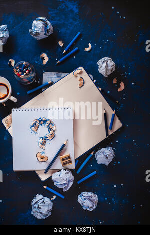 Creative block concept. Question mark from pencil shavings with crumpled paper balls, pencils, notepads and empty coffee cups. Still life with writer workplace. Stock Photo