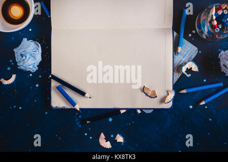Writers block concept with open notepad, empty coffee cups, pencils and crumpled paper balls on a dark background. Creative workplace. Editing and copywriting concept. Stock Photo