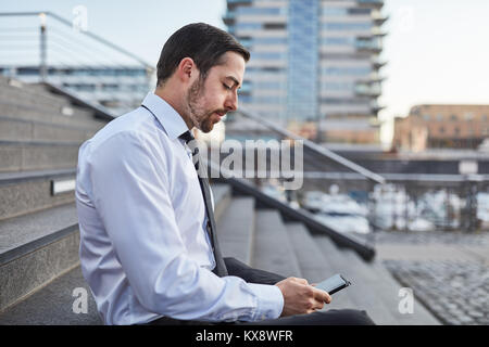 Young business man using app on smartphone outside Stock Photo