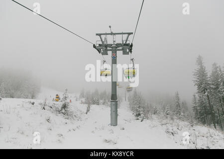 Ski chairlift bringing skiers and snowboarders up the Skrzyczne mountain after heavy snowfall on a misty winter day in Szczyrk ski resort in Poland Stock Photo