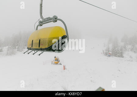 Ski chairlift bringing skiers and snowboarders up the Skrzyczne mountain after heavy snowfall on a misty winter day in Szczyrk ski resort in Poland Stock Photo